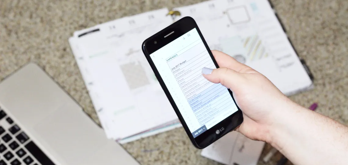 woman holding a smart phone with a budget sheet on the screen