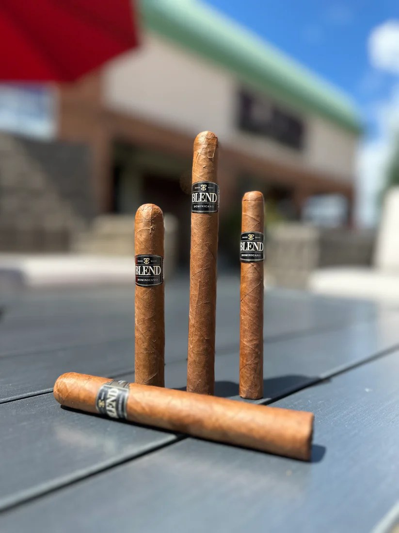 Blend Cigar IMG_4142 Cigars standing on end on a table outdoors with the front of Blend Cigar blurred in the background.