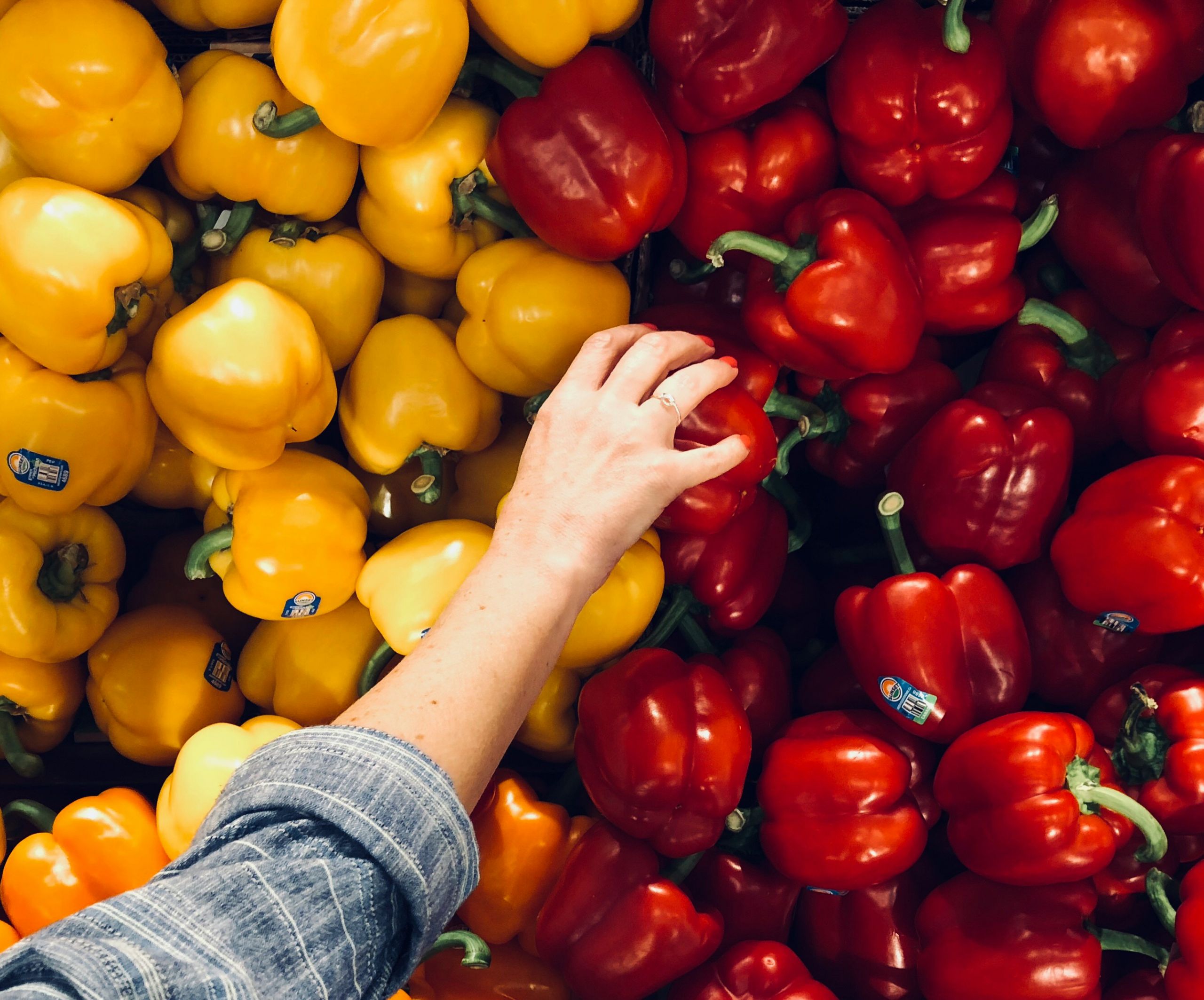 Hand reaching for red bell pepper with a pile of yellow bell peppers next to it.