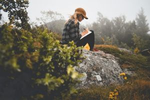 A girl sitting on a rock, writing.