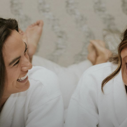 Two people laughing in a bed wearing robes.