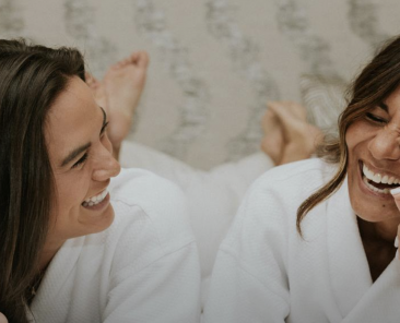 Two people laughing in a bed wearing robes.