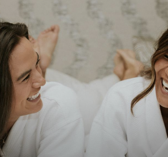Two people laughing in a bed wearing robes.