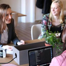 Three women talking in an office space, discussing business.