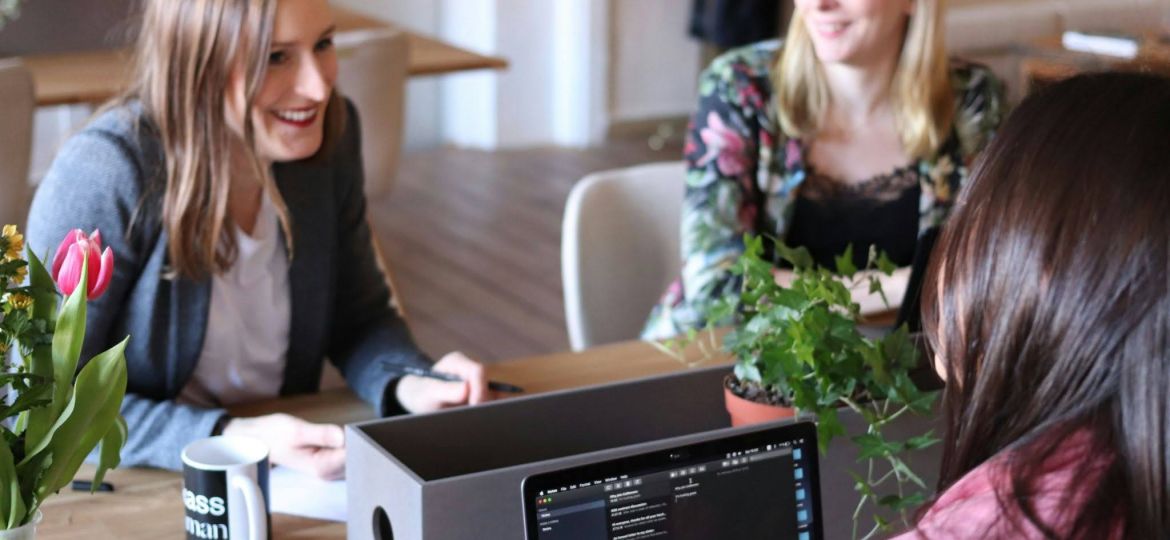 Three women talking in an office space, discussing business.