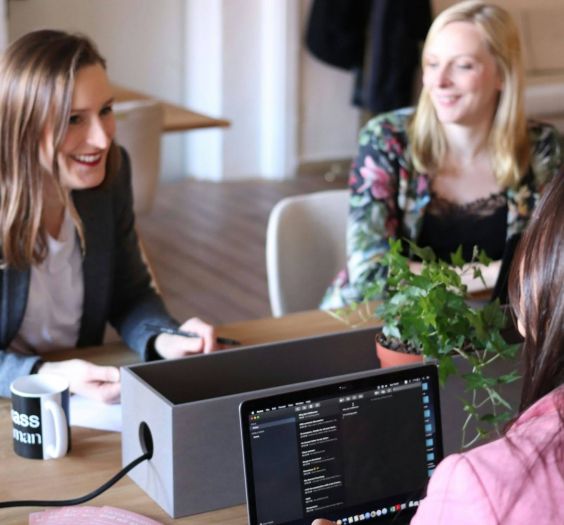 Three women talking in an office space, discussing business.