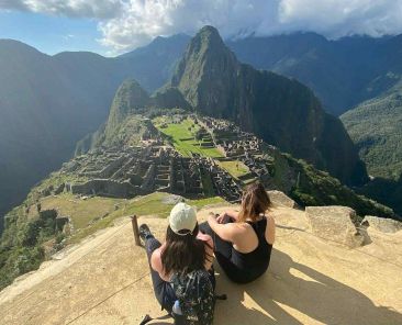 2 women sitting on a peak surrounded by mountains in Peru