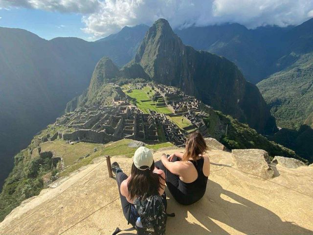 2 women sitting on a peak surrounded by mountains in Peru