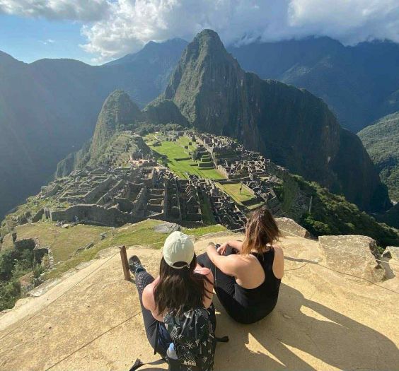 2 women sitting on a peak surrounded by mountains in Peru
