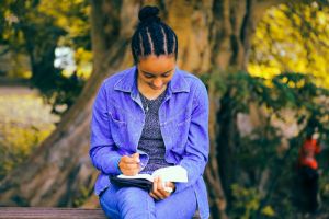 a woman sitting on a bench writing in a notebook