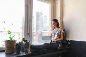 a woman sitting next to a window working on a tablet