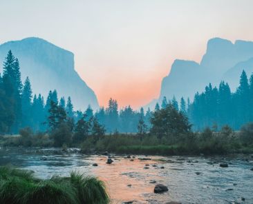 landscape image with a lake, trees, mountains in the distance and a sunset