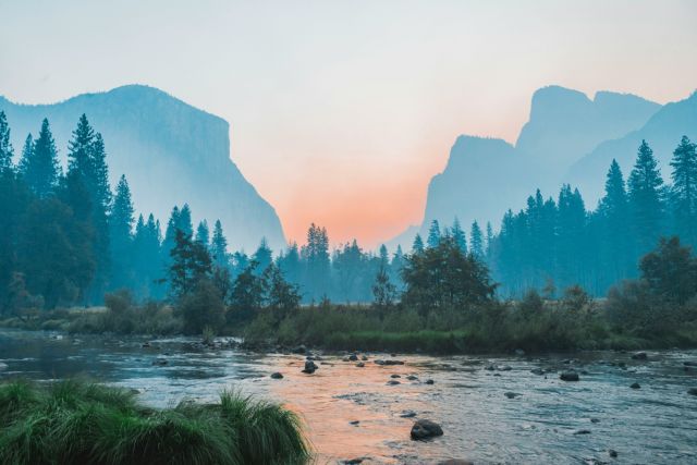 landscape image with a lake, trees, mountains in the distance and a sunset