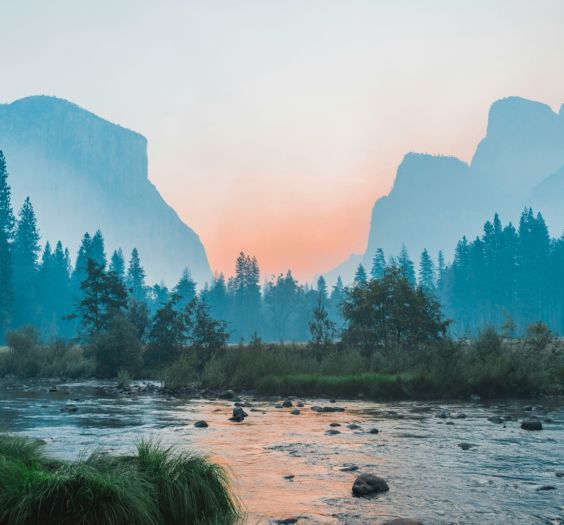 landscape image with a lake, trees, mountains in the distance and a sunset