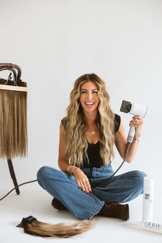 Lindsay Stafford_TheBurgundy Lindsay Stafford of the Burgundy sitting cross-legged on the floor with extensions and holding a hair dryer